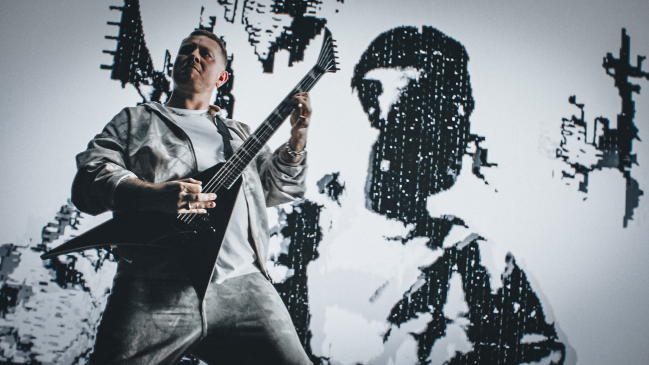 Musician performing with a satin black Jackson Pro Plus Pure Metal Stealth guitar onstage in front of a high-contrast digital backdrop