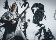 Musician performing with a satin black Jackson Pro Plus Pure Metal Stealth guitar onstage in front of a high-contrast digital backdrop