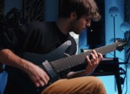 Musician playing an Ibanez Alpha extended-range electric guitar with headstock in a blue-lit studio