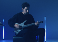 Plini playing his Strandberg Boden Standard NX 6 Plini Edition Mirage signature electric guitar under blue stage lighting.