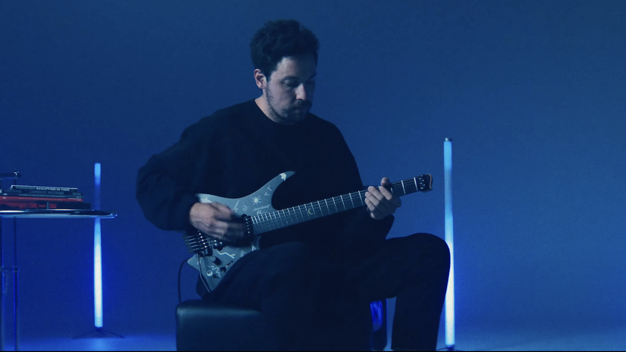 Plini playing his Strandberg Boden Standard NX 6 Plini Edition Mirage signature electric guitar under blue stage lighting.