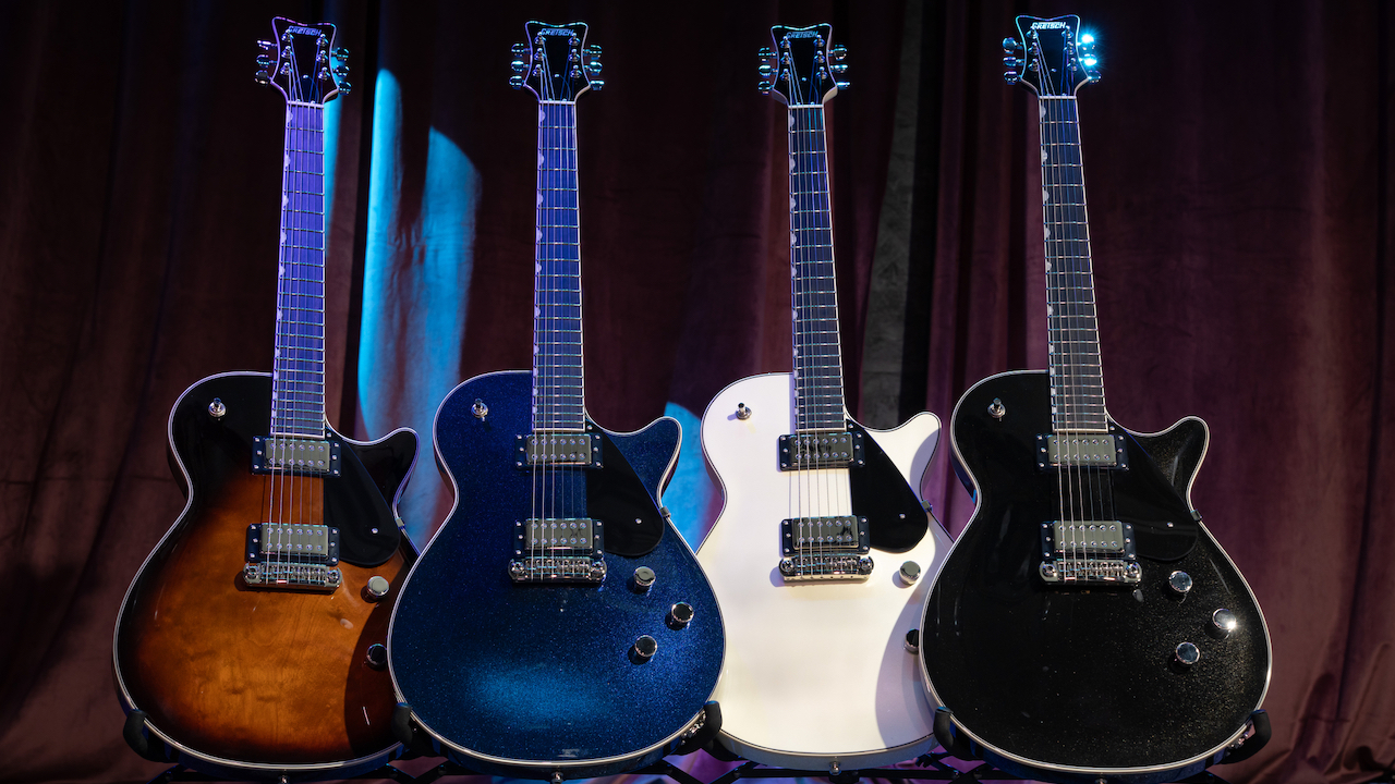 Four Gretsch Electromatic Premier Jet electric guitars in different finishes displayed on stands against a stage curtain backdrop.