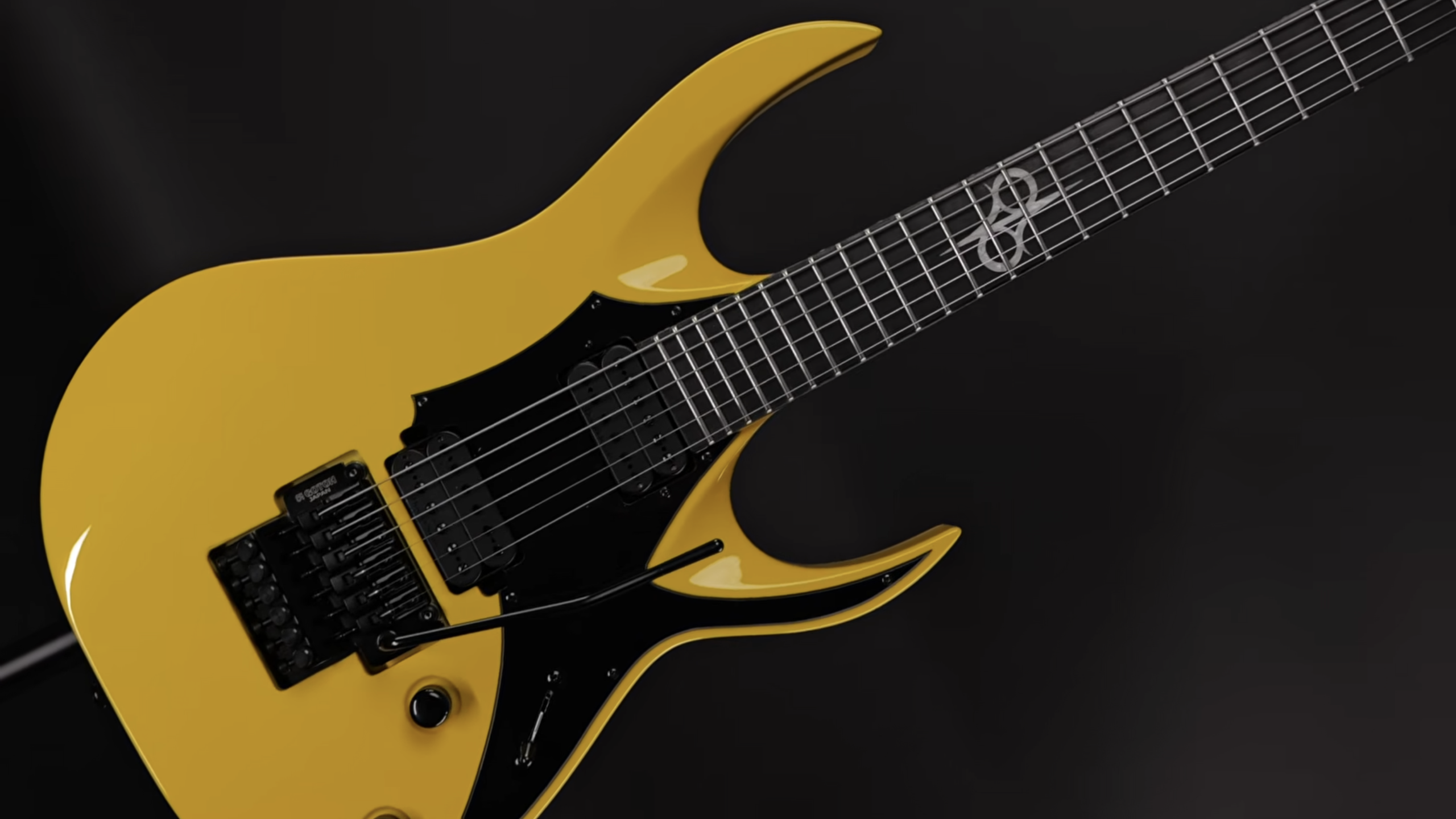Yellow solid-body electric guitar with black pickguard, dual humbuckers, and a Floyd Rose-style tremolo bridge against a dark background.