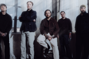 Erra band members posing in a softly lit industrial room with sheer curtains and natural light.