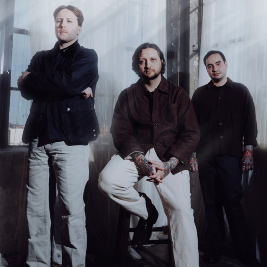 Erra band members posing in a softly lit industrial room with sheer curtains and natural light.