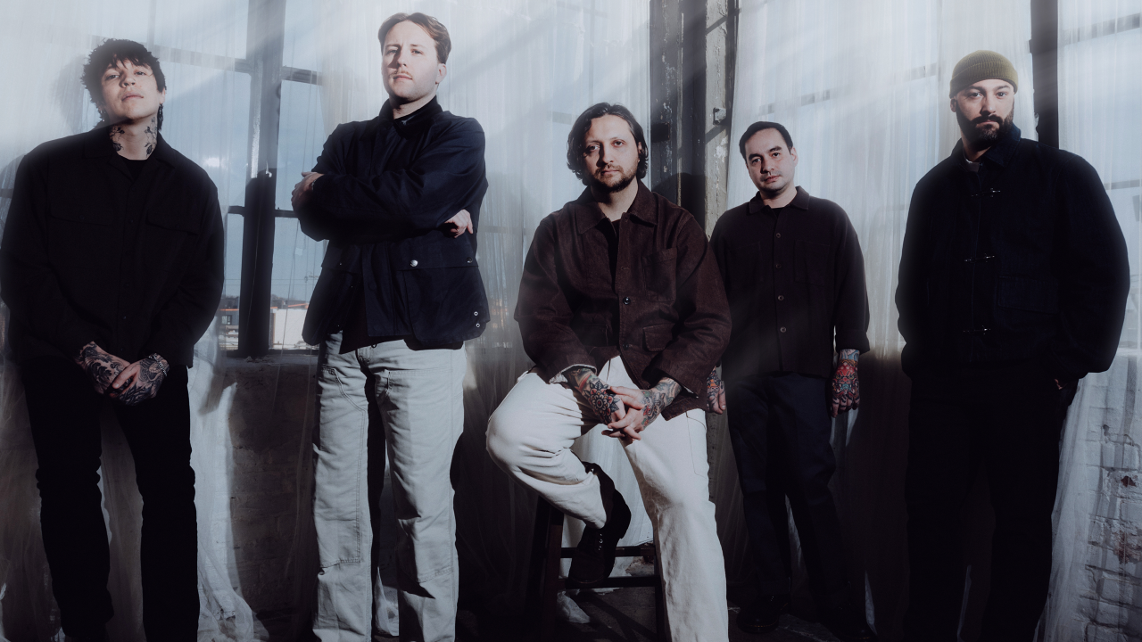 Erra band members posing in a softly lit industrial room with sheer curtains and natural light.