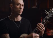 Matt Heafy holding an Epiphone Les Paul Custom guitar during an interview or studio session.