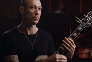 Matt Heafy holding an Epiphone Les Paul Custom guitar during an interview or studio session.