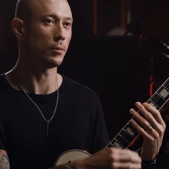 Matt Heafy holding an Epiphone Les Paul Custom guitar during an interview or studio session.