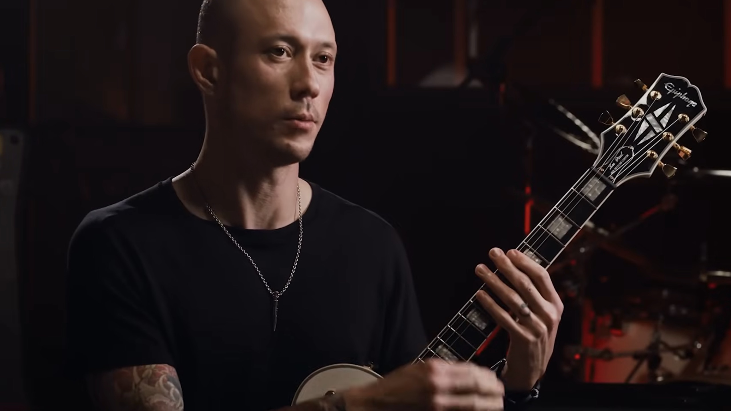 Matt Heafy holding an Epiphone Les Paul Custom guitar during an interview or studio session.