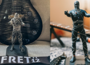 String Thing mummy figurine wrapped in recycled guitar strings displayed in front of an electric guitar.