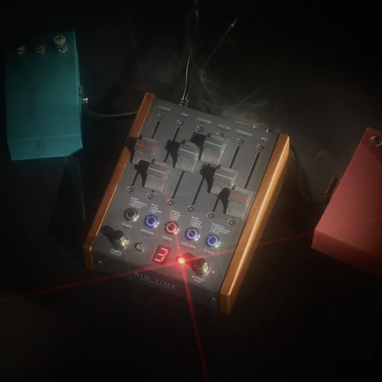 Studio photo of a boutique stereo delay guitar pedal with wooden sides and multiple sliders, glowing LED indicators, and connected cables, surrounded by two smaller effects pedals in teal and red on a dark background with dramatic lighting.