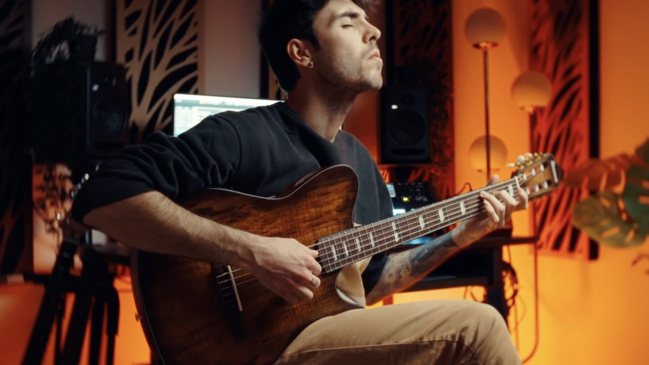 Musician playing an Ibanez FRH20 nylon-string electric-acoustic guitar in a warmly lit recording studio with studio monitors and ambient orange lighting in the background.