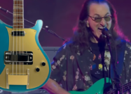 Geddy Lee performing live on stage beside a photoshopped image of his new Rickenbacker bass guitar, highlighting the instrument’s design and finish.