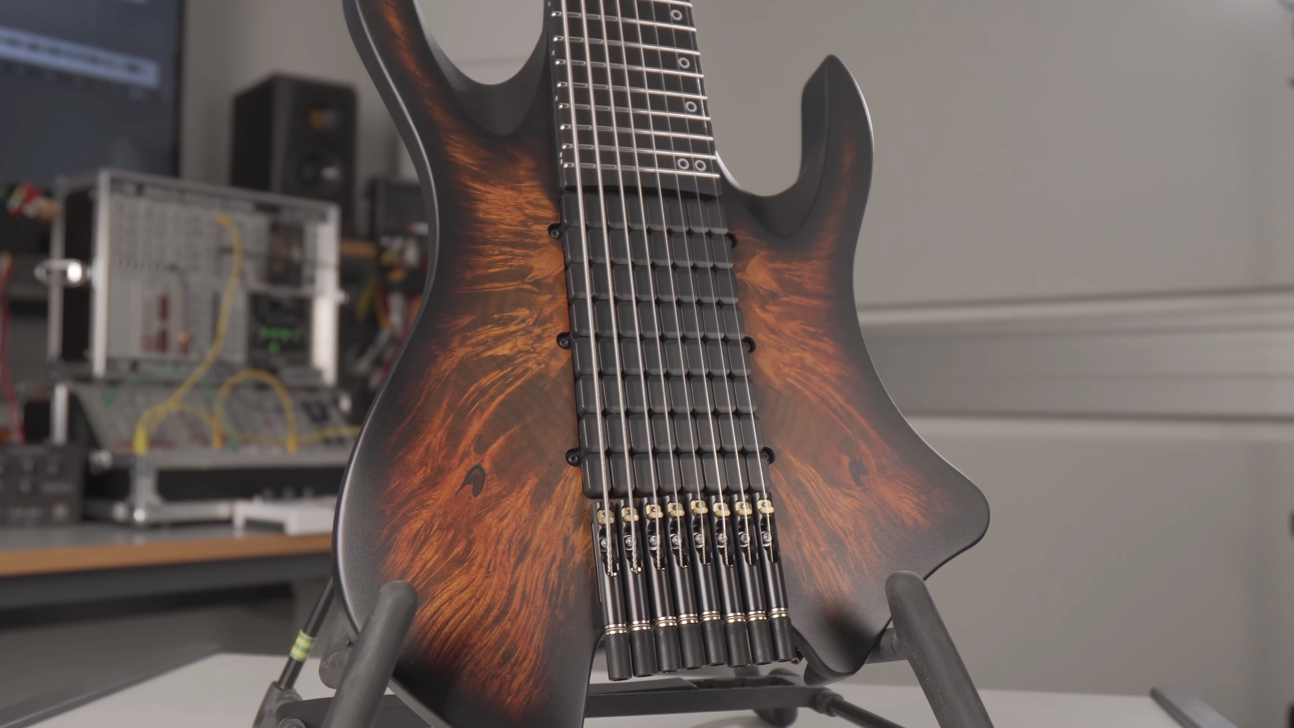 Close-up of a PolyMap electric guitar with a multi-scale fretboard and a dark burst finish, resting on a stand.