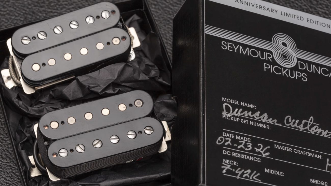 Close-up of a limited-edition Seymour Duncan 50th Anniversary Duncan Custom pickup set resting in black packaging beside the commemorative box. The image shows two humbucker pickups with black bobbins, exposed pole pieces, and vintage-style detailing, highlighting the hand-built Custom Shop presentation.