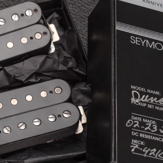 Close-up of a limited-edition Seymour Duncan 50th Anniversary Duncan Custom pickup set resting in black packaging beside the commemorative box. The image shows two humbucker pickups with black bobbins, exposed pole pieces, and vintage-style detailing, highlighting the hand-built Custom Shop presentation.