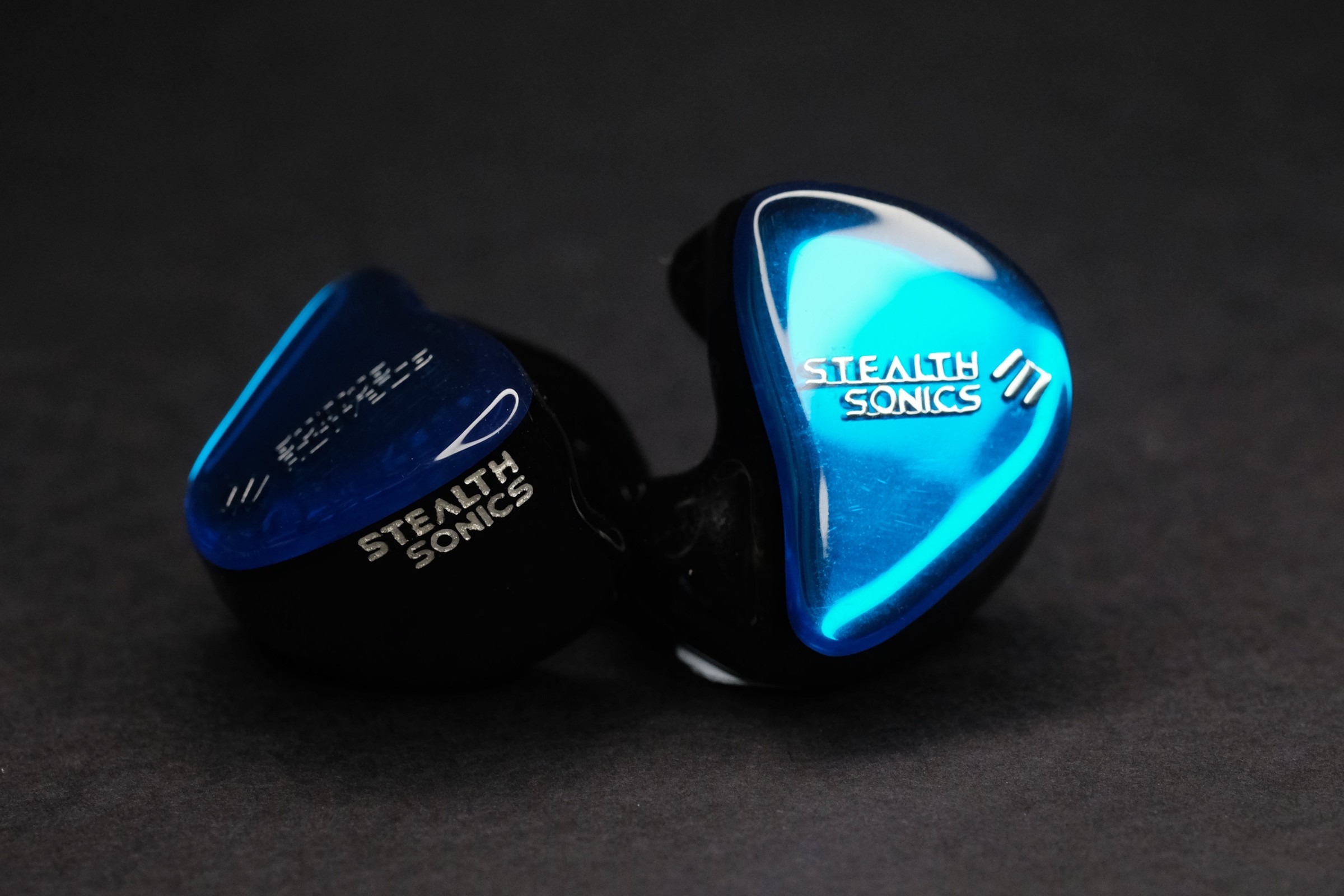 Pair of Stealth Sonics custom in-ear monitors with glossy blue faceplates and Stealth Sonics logos on a dark background